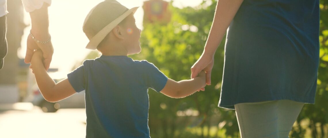 A family with a young child holding hands outdoors.