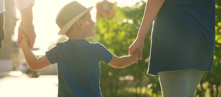 A family with a young child holding hands outdoors.