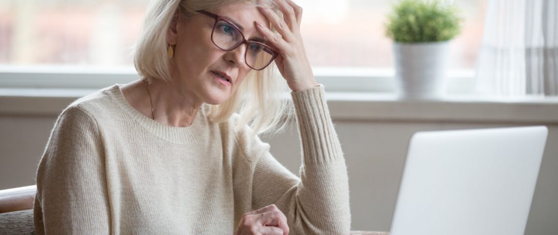 A retired woman looking worried while using a laptop.