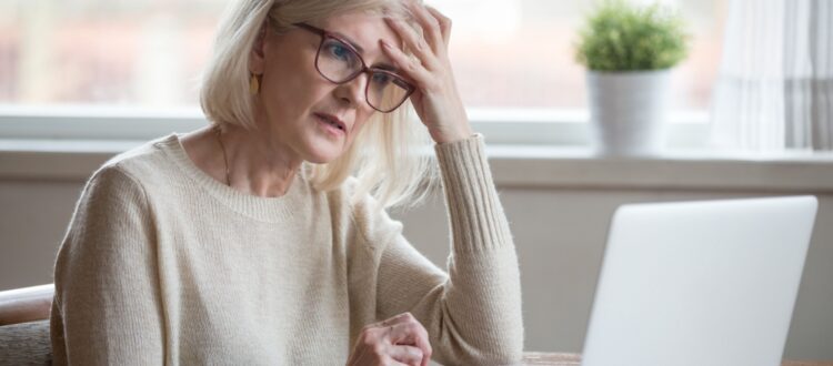 A retired woman looking worried while using a laptop.