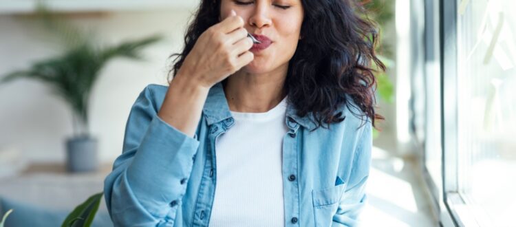 A woman eating a pot of yoghurt.