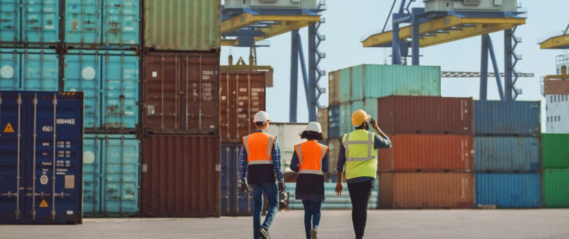Workers walking through a shipping cargo container terminal depot.
