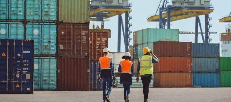 Workers walking through a shipping cargo container terminal depot.