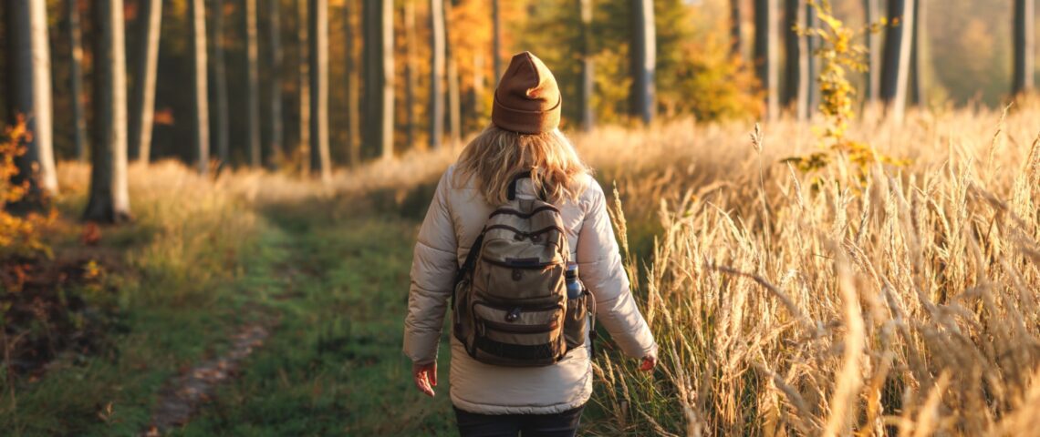A woman with a backpack walking through woodland.