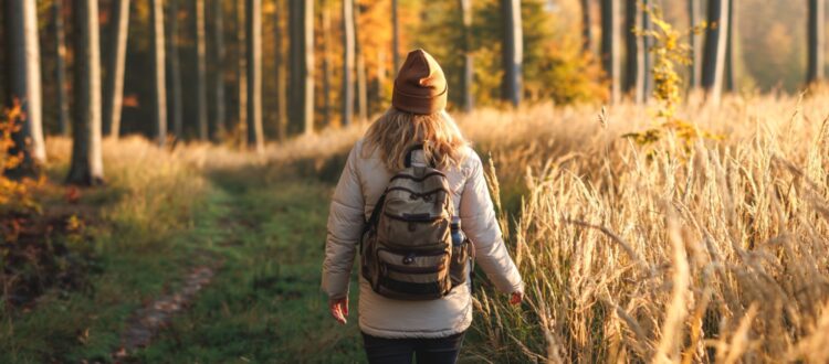 A woman with a backpack walking through woodland.