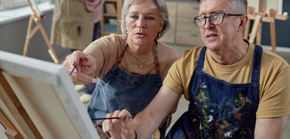 An older couple painting at an easel together.