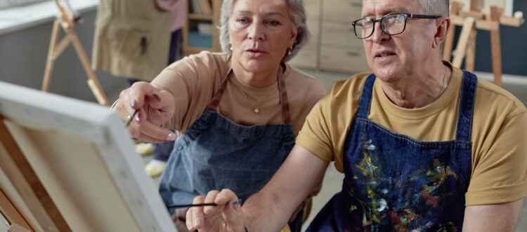 An older couple painting at an easel together.