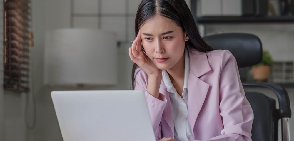 A woman at her computer, thinking carefully.