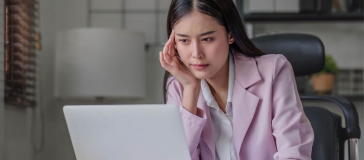 A woman at her computer, thinking carefully.