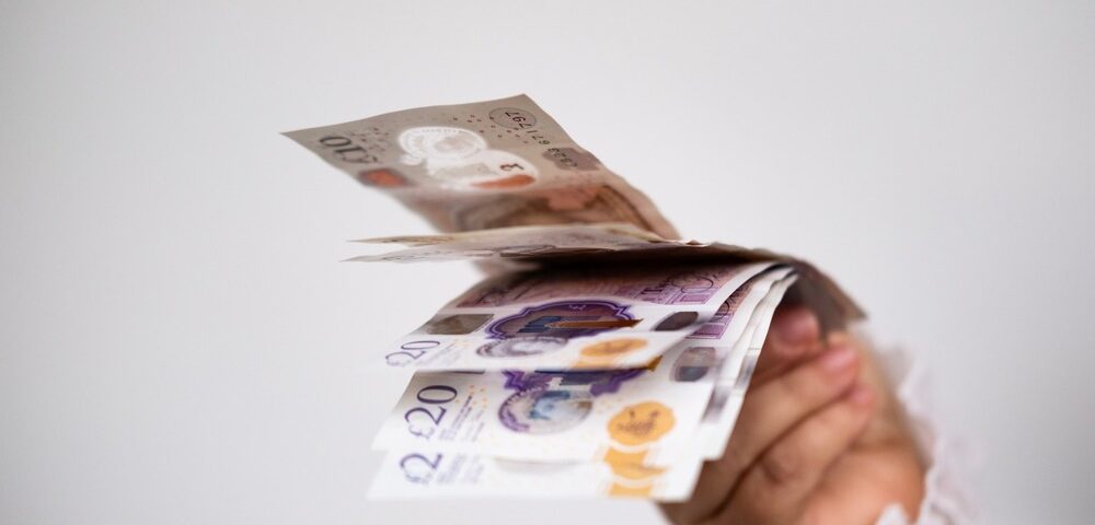 A hand holding UK bank notes.