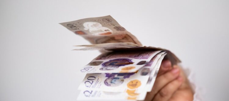 A hand holding UK bank notes.