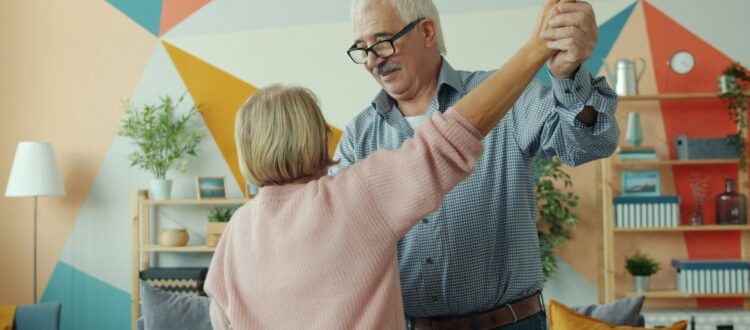 Two happy pensioners dancing at home, holding hands and having fun
